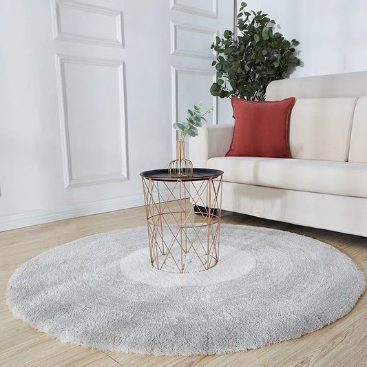 Round gray rug in a living room with a white sofa, red pillow, and a small table.