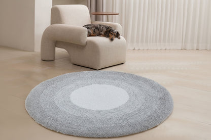 Round gray rug with a white center in front of a beige armchair.