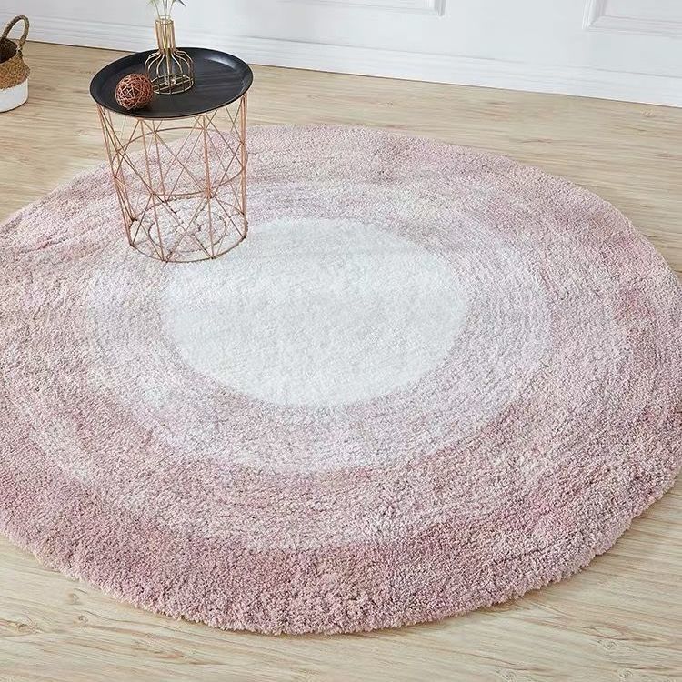 Round pink and white gradient rug on a wooden floor with a small table.