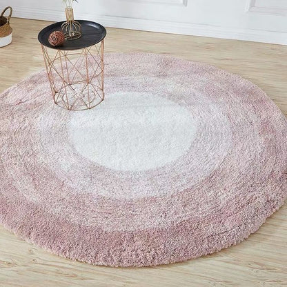 Round pink and white gradient rug on a wooden floor with a small table.